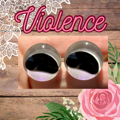 Two spherical objects, resembling safety eyes for amigurumi with a reflective black surface at their centers, are displayed against a floral and wooden background. 